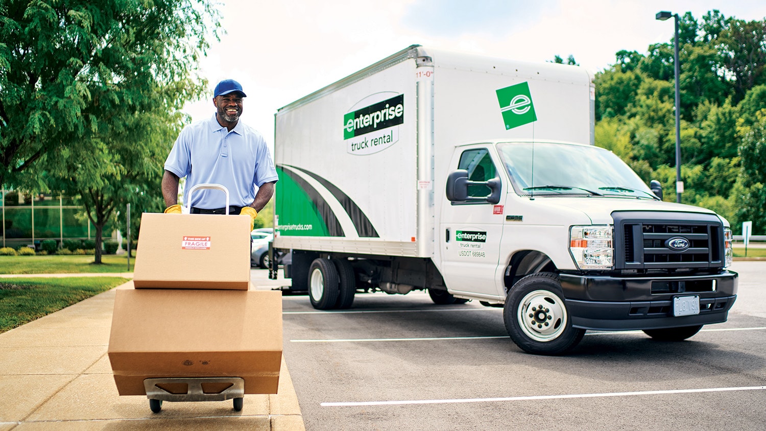 Man pushing boxes on a hand truck in front of an Enterprise Parcel Van